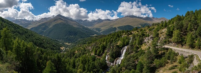 Panoramic shot of a mountain range with green trees, waterfalls, blue sky, and white clouds on a sunny day