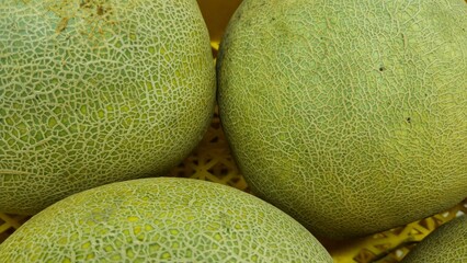 Close-up of several green melons with rough netted skin texture, placed inside a yellow basket at a market or store.  
