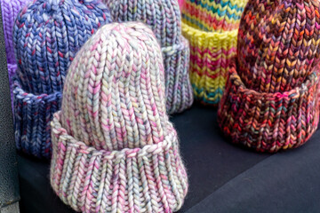 Colorful knitted winter hats in various shades and patterns, neatly arranged on a black display background.