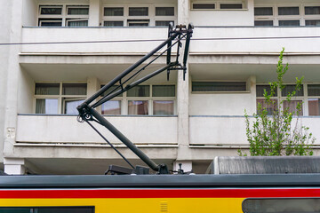 Tram pantograph raised above vehicle roof near residential building with balconies and windows.