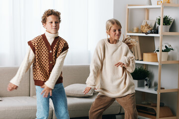 Fototapeta premium Authentic scene of playful movement at home, featuring a school aged child and adult dancing, casual knitwear, candid moment, wholesome lifestyle.