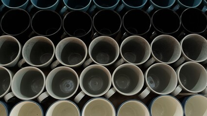 Top view of multiple ceramic mugs neatly arranged in rows, creating a repetitive pattern with...