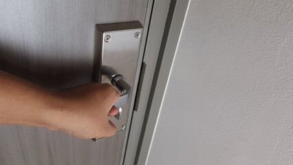 A person’s hand gripping a silver metal door handle, about to open a wooden door, showing entry,...