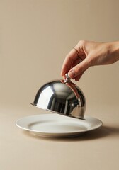 Unveiling Culinary Surprise: An elegant hand lifts a gleaming silver cloche, offering a tantalizing glimpse of the culinary delight it conceals, presented on a pristine plate.