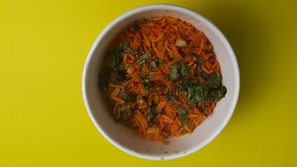 Top view of a white bowl filled with biryani rice garnished with herbs, placed against a vibrant yellow backdrop.
