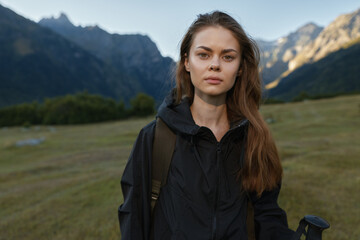 Naklejka premium A confident traveler stands outdoors in a rugged mountain landscape, wearing a black jacket and backpack, looking directly at the camera with calm resolve and poised presence.