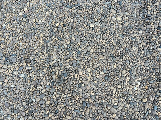 A close-up, top-down view of a collection of small, smooth river stones or pebbles. The stones vary in color, primarily featuring shades of gray, tan, and brown.