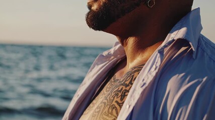 Close up of a rugged, bearded man with a chest tattoo savoring the soft sunset light by a serene ocean, evoking a sense of liberation and peace