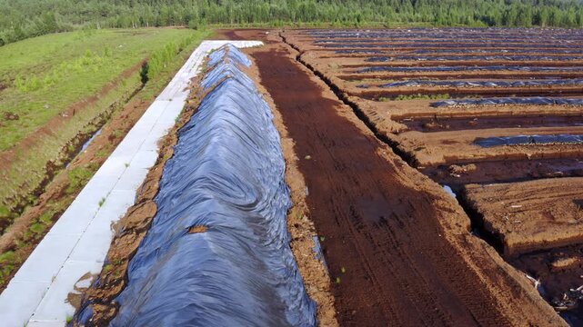 Drone moving forward. Aerial view. Flight over a large peat pile covered with polyethylene film to protect the peat from rain. Turf mining industry.