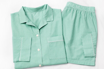 Green striped Pajama Set on white sheet background. Top view home sleepwear female from soft cotton trend mint green colored on bedclothes. Cozy pyjamas of shirt and shorts for comfort rest, flatly