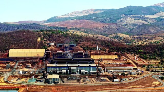 Nickel mining facility in Brazil, showing large industrial structures, processing plants, and surrounding mountain terrain under clear skies, aerial view