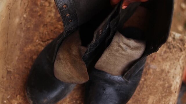 Hand placing worn black boots on a curb