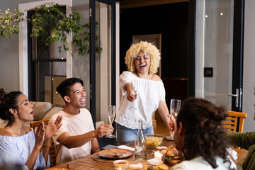 Diverse friends celebrating at dinner table, raising glasses and laughing together