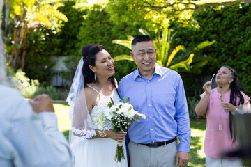 Celebrating senior wedding in garden, bride and groom smiling with family outdoors