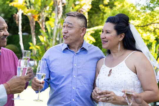 Celebrating outdoor senior wedding, senior couple holding champagne glasses and smiling with friends - Powered by Adobe