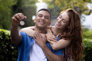 Young couple outdoors holding keys, smiling and celebrating new home together