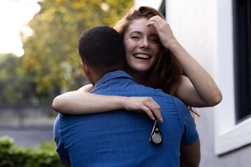 Young couple embracing outdoors, woman smiling joyfully while holding keys