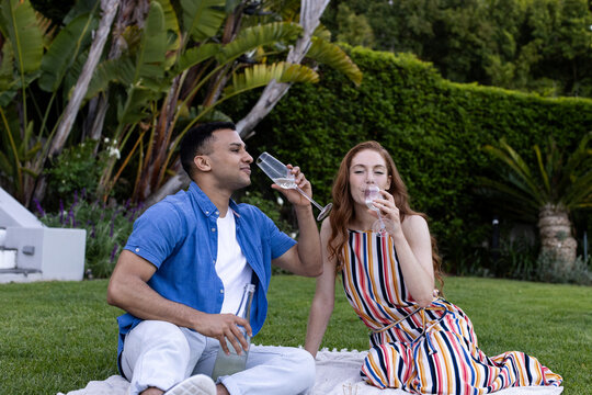 Young couple enjoying drinks on picnic blanket in lush garden setting