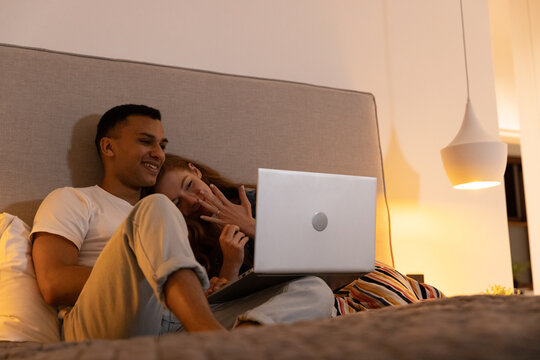 Young couple relaxing in bed, watching laptop together, enjoying cozy evening