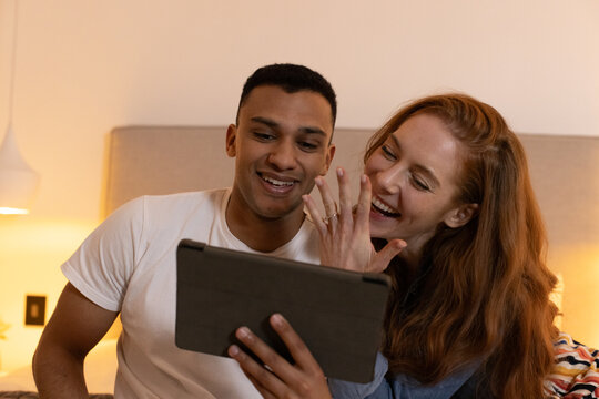 Young couple laughing while watching tablet together in cozy bedroom
