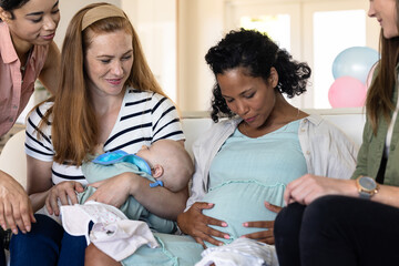 Celebrating baby shower, friends admiring pregnant woman and smiling at home gathering