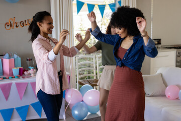Friends celebrating at home, dancing joyfully with colorful balloons and decorations © wavebreak3