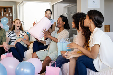 Women celebrating baby shower at home, opening gifts and enjoying together