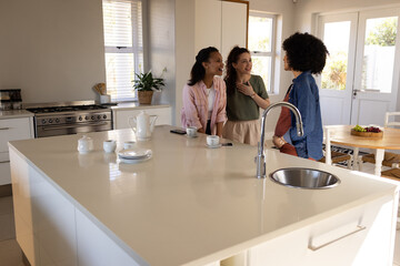 Friends chatting and enjoying coffee together in modern kitchen, sharing laughter