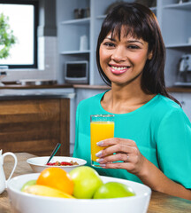 Smiling woman enjoying healthy breakfast with orange juice in modern kitchen
