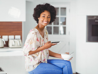 African American woman enjoying breakfast while using smartphone in modern kitchen