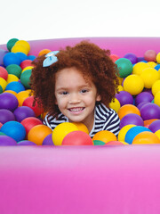 Smiling child playing in colorful ball pit, enjoying fun indoor activity