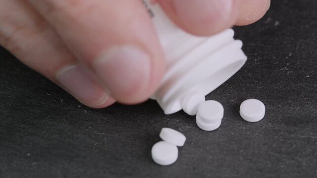 Hand poured sugar substitute tablets from a plastic bottle onto a black surface. Artificial sweetener pills zero calories