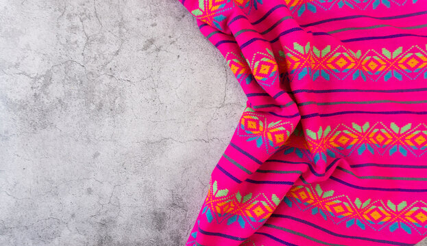 Top view of a pink Mexican tribal fabric with small folds on a gray surface