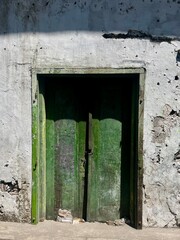 An old green wooden door, with peeling paint and a broken door lock.