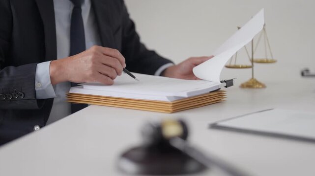 Adult Asian lawyer examining legal documents in office diligent professional works on important case with justice scales and gavel present