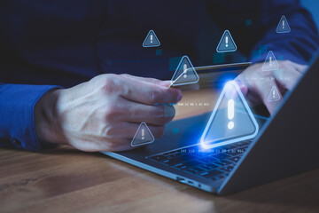 Person holding a credit card while using a laptop computer with warning symbol, representing online payment risk, online shopping, financial fraud, and identity theft during digital transactions.