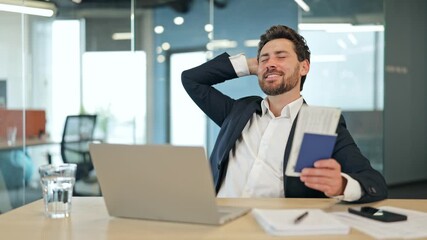 Successful businessman in a stylish suit and white shirt, happily planning an upcoming vacation. Sitting in a modern office, he holds a passport and tickets, dreaming of travel and relaxation.