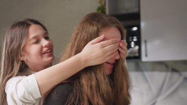 Buddy in kitchen as friend covers eyes playfully then releases both laugh warm candid moment soft daylight on hair casual home scene hands over face joyful surprise domestic fun genuine reaction