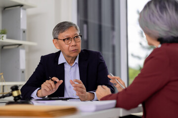Experienced Asian legal advisor discusses case with client in professional office setting providing...