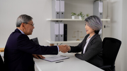 Asian legal professionals shaking hands reaching business agreement in modern law office demonstrating trust and successful negotiation client meeting