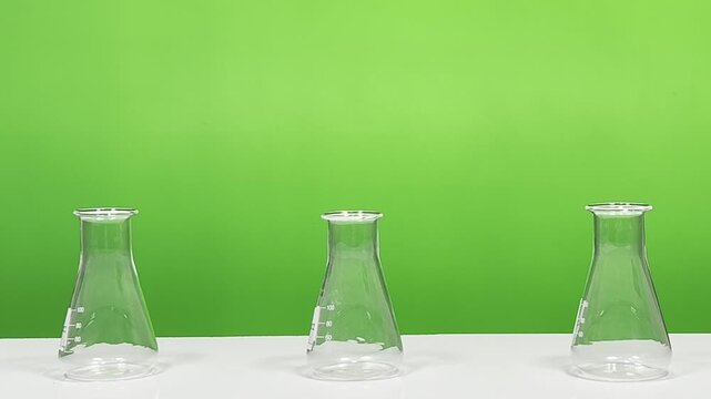 Three empty Erlenmeyer flasks on white surface with green background