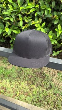 Black trucker cap hanging on a iron fence, with a natural green leaves background.