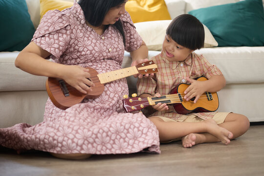 A mother and child playing a ukulele together in a cozy living room setting