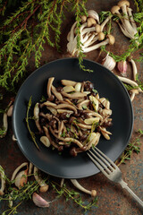 Fried shimeji mushrooms with thyme and garlic on a black plate.