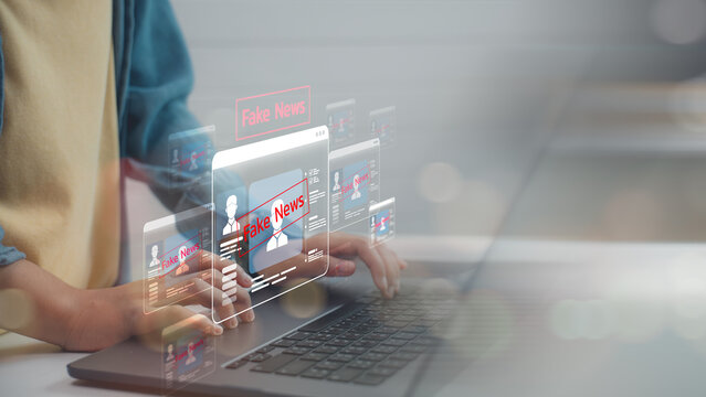 Person using a laptop with digital fake news alerts on screen. Concept of misinformation, social media hoaxes, online disinformation, and the fight against digital deception.