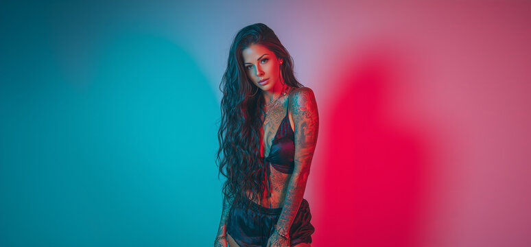 Captivating model with tattoos in a striking blue and red light, showcasing confidence and allure in a stylish outfit during a modern studio photoshoot