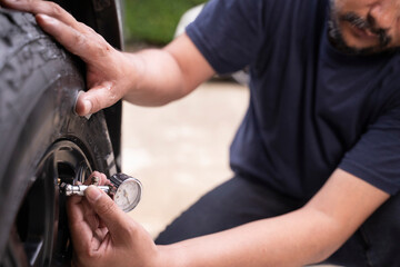 Photo of a young man checking the air pressure in his car tires by himself.