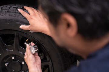 Photo of a young man checking the air pressure in his car tires by himself.