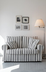 a white-striped sofa, with small black-and-white photo posters on the wall behind it, a floor lamp beside the sofa, the sofa in front of the camera, a simple living room background, white walls