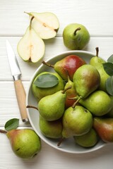 Fresh ripe pears, knife and green leaves on white wooden table, flat lay